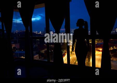 The silhouette of a girl against a stained-glass window looks at the night city. Stock Photo