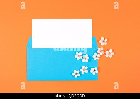 Blue envelope with white card and flowers on orange background. Top view. Copy space. Stock Photo