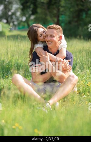 Cute young couple sitting on grass, kissing. Young man and woman enjoying summer day. Happy people in love, honey moon Stock Photo