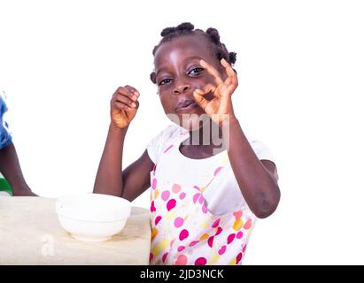 cute little girl sitting at a table facing a cup of coffee, and making a correct gesture. Stock Photo