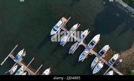 A direct overhead aerial photo above a sunny dock filled with moored leisure craft and yachts are seen below at dusk. Stock Photo