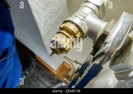 Stuttgart, Germany - February 01, 2022: Hand replace old danfoss radiator thermostat valve. Pliers removes component from the heater. Modernization of Stock Photo
