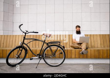 Smiling mid adult man using laptop while sitting on bench Stock Photo