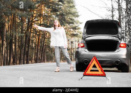 Red emergency triangle on the road with a blurry car in the background and a desperate woman catching passing cars waiting for help. Focus on Stock Photo