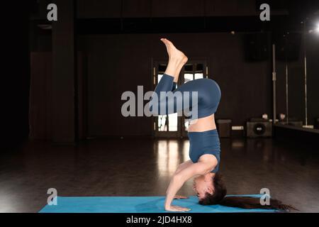 Side view of hispanic woman doing yoga exercise at gym,yoga forearm stand pose or Pincha Mayurasana.Calm healthy young female breathing and meditate Stock Photo