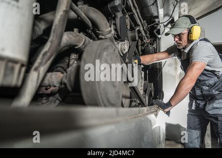 Caucasian Technician in Safety Headphones Thoroughly Checking the Condition of the Engine in the Bus During Annual Inspection. Automotive Industry The Stock Photo