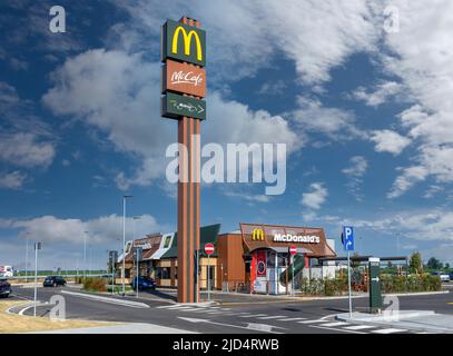 Savigliano, Italy - June 16, 2022: new McDonald's restaurant with large tall totem sign with McCafè logo and McDrive on blue sky with white clouds, Mc Stock Photo
