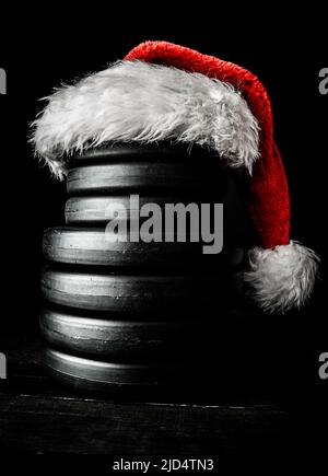 Gym dumbbell barbell weight plates stacked on top of each other in shape of a snowman, with red Santa Claus hat. Healthy fitness Christmas concept. Stock Photo