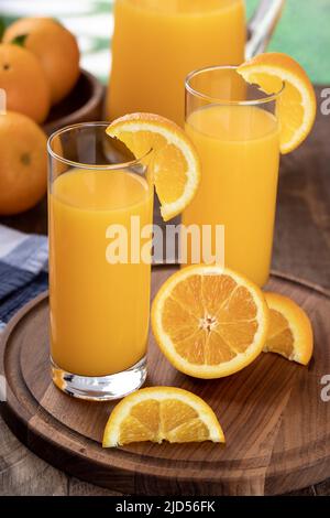 Two glasses of orange juice with sliced oranges on a wooden tray and pitcher in background Stock Photo