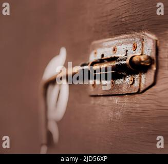 There is a rusty old latch on the brown old door. The mechanism for closing the door. Stock Photo
