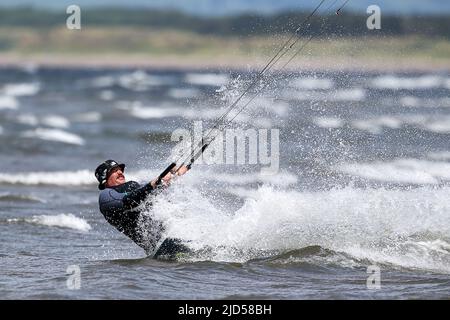 Troon, UK. 18th June, 2022. Strong winds, high waves and sunshine made ideal conditions for the kitesurfing and water sports enthusiasts as they take advantage of the summer weather on the Firth of Clyde, off South Beach, Troon, Scotland, UK. Credit: Findlay/Alamy Live News Stock Photo