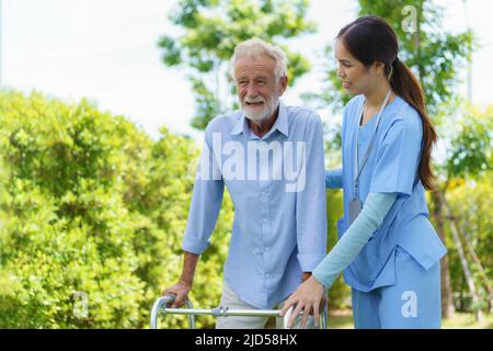 Young Asian woman nurse care giver helping senior old man with mobility walker in garden at home. Senior daycare center, Nurse take care elderly patie Stock Photo