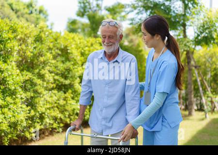 Young Asian woman nurse care giver helping senior old man with mobility walker in garden at home. Senior daycare center, Nurse take care elderly patie Stock Photo