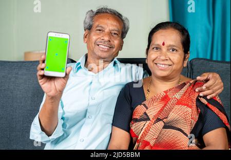 Happy smiling senior couple showing green screen mobile phone by looking at camera - concept of technology, application and togetherness Stock Photo