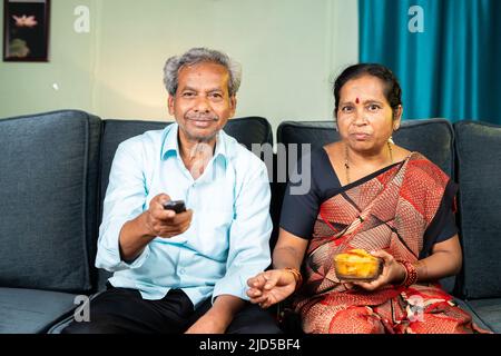 Senior couple watching tv or television at home by surfing channels - concept of relaxation, leisure activities and entertainment Stock Photo