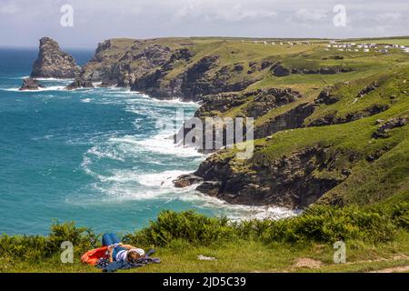 A young woman lies down beside the cliff over looking the ocean from the South West Coast Path close  to Tintagel Cornwall England UK Stock Photo