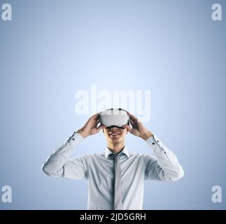 Virtual reality concept with young businessman gets new emotions in VR glasses on abstract light blue background and empty space on his head for you t Stock Photo