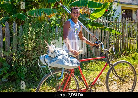 A young man coming from spearfishing and bringing his catch home by bicycle near Baracoa, Cuba Stock Photo