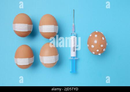 flatlay with monkeypox vaccine syringe and vaccinated eggs with medical patch and egg with monkeypox symptoms on blue background. Stock Photo