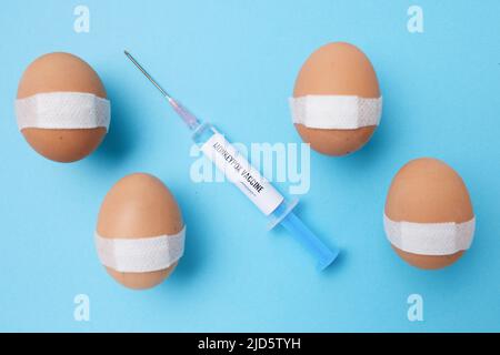 flatlay with monkeypox vaccine syringe and vaccinated eggs with medical patch on blue background. Stock Photo