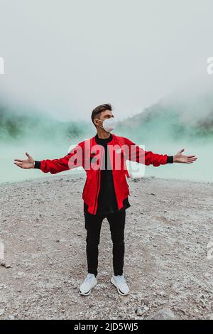 young man in red bomber jacket standing at kawah putih sulfer lake in Bandung Stock Photo