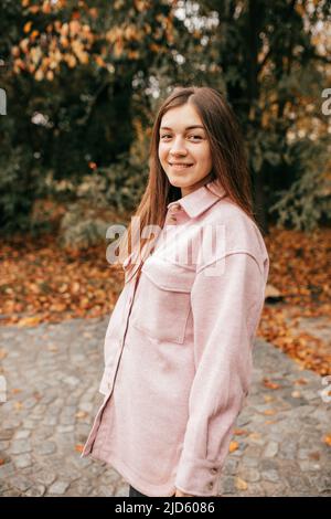 Charming brown-haired woman walking on warm autumn day in city square looks happy and peaceful. She is wearing warm soft pink shirt. Weekend Stock Photo