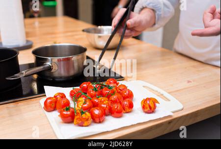 https://l450v.alamy.com/450v/2jd628y/a-person-uses-culinary-tongs-to-pull-out-of-boiling-oil-cherry-tomatoes-and-places-them-on-the-board-to-cool-down-and-to-pill-off-the-skin-2jd628y.jpg