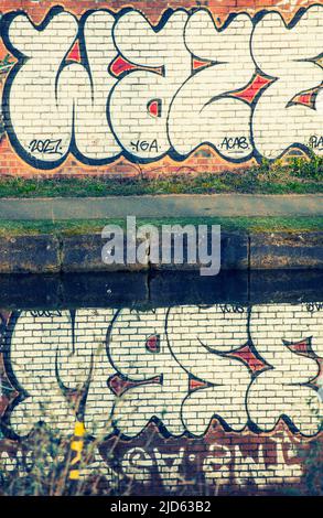 Graffiti on a brick wall reflected in the water of the Bridgewater Canal in Stretford, Manchester, England, UK Stock Photo