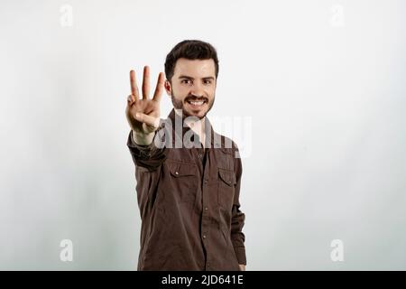 Happy young man wearing shirt posing isolated over white background showing and pointing up with fingers number three while smiling. Stock Photo