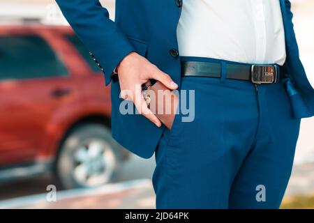 A businessman in a blue suit get a leather key bag from the pants. Defocused car on the background. Close-up of the hands. The concept of style and fa Stock Photo