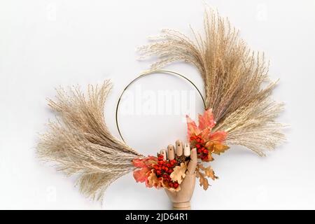Dried floral wreath from dry pampas grass and Autumn leaves. Fall fecorations tied with cord to metal frame. Fig fruits on off white background. Stock Photo