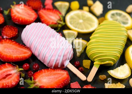 Two ice creams on a sticks - strawberry and lemon on a black background. Summer fruit desserts. Stock Photo