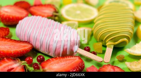 Two ice creams on a sticks - strawberry and lemon on a green background. Summer fruit desserts. Stock Photo
