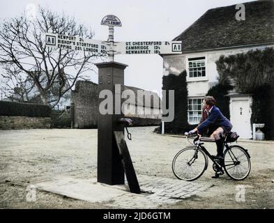 The old-time centre of village life is the 'Village Pump' at Littlebury, Essex, England. This pump is still in use and is being admired by a young man on a bicycle! Colourised version of : 10185331       Date: 1940s Stock Photo