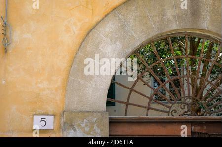 Rusted iron grate set in arched doorway with simple address on plaster wall. Stock Photo