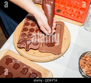 The chef's hands pour hot chocolate into silicone molds using cooking envelopes. Stock Photo