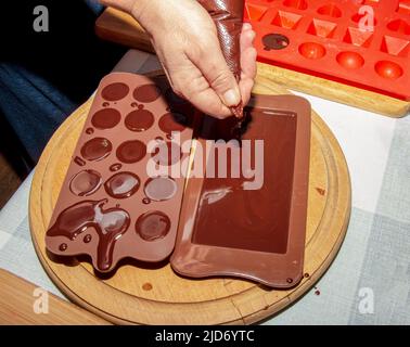 The chef's hands pour hot chocolate into silicone molds using cooking envelopes. Stock Photo
