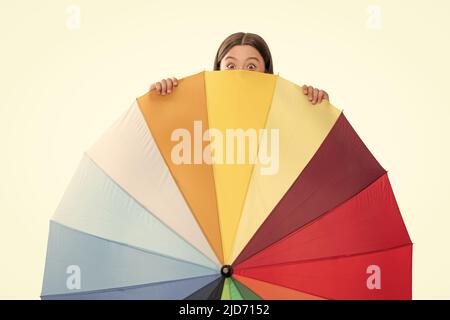 child hiding behind colorful parasol. kid with rainbow umbrella isolated on white. Stock Photo