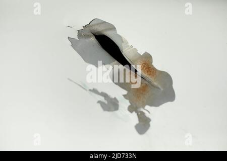 Hole in metal. Damaged steel with white paint. Broken surface of car. Damage to vehicles. Stock Photo
