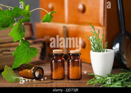 Bottles of homeopathy granules, cabinet with homeopathic remedies and old books on background. Homeopathy medicine concept. Stock Photo