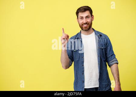 Smiling man raised finger up as sign he has new idea on yellow studio background Stock Photo