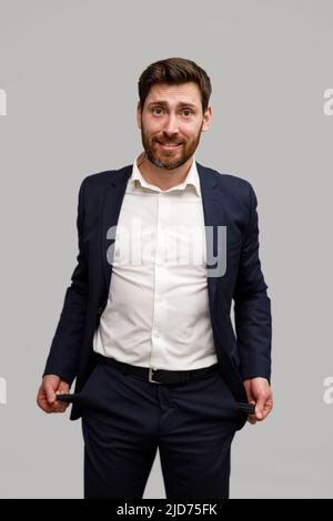 Businessman showing his empty pockets standing on grey studio background Stock Photo