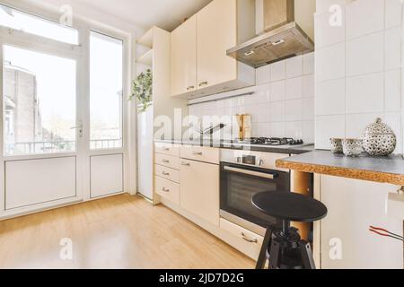 Interior of bright kitchen with wooden floor, cabinets and balcony doors in modern apartment during daytime Stock Photo