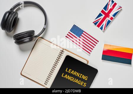 Learning foreign languages. Audio language courses. Background from countries flags and headphones white on the table. Stock Photo