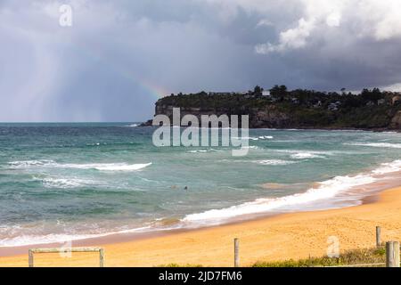 Moody sky and rainbow over Avalon Beach Sydney on a winters day as stormy weather closes in,Sydney,NSW,Australia Stock Photo