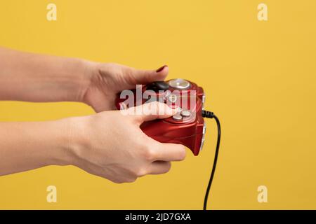 Profile side view closeup portrait of woman hand holding red gamepad joystick for playing video game. Indoor studio shot isolated on yellow background. Stock Photo