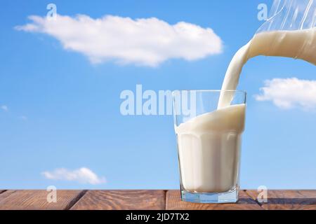 milk pouring from jug into glass on table Stock Photo