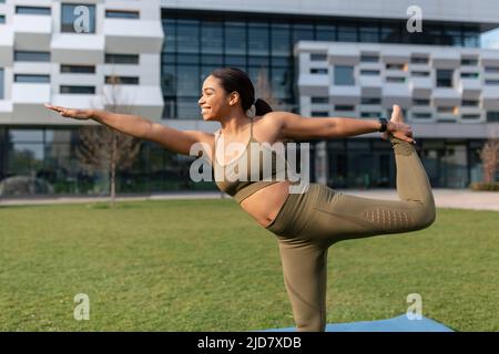 Young black woman in sportswear practicing yoga or pilates, stretching her body outdoors Stock Photo