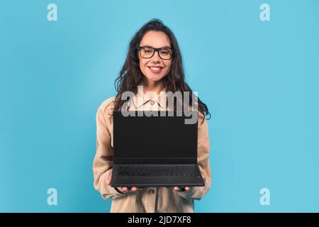 Glad smiling millennial european lady brunette student in casual and glasses showing laptop with blank screen Stock Photo