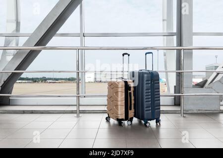 Two Stylish Plastic Luggage Suitcases Standing Near Panoramic Window At Airport Stock Photo